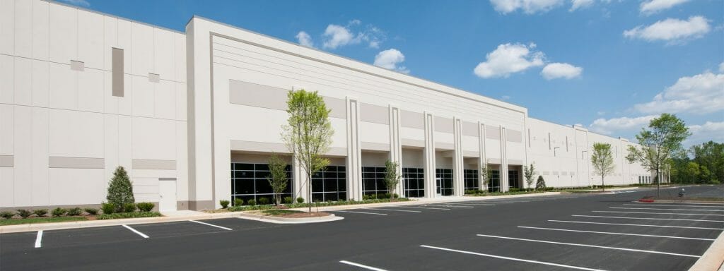 DSC_0476_small Modern warehouse exterior with large windows, an empty parking lot, cloudy sky, and minimal landscaping.