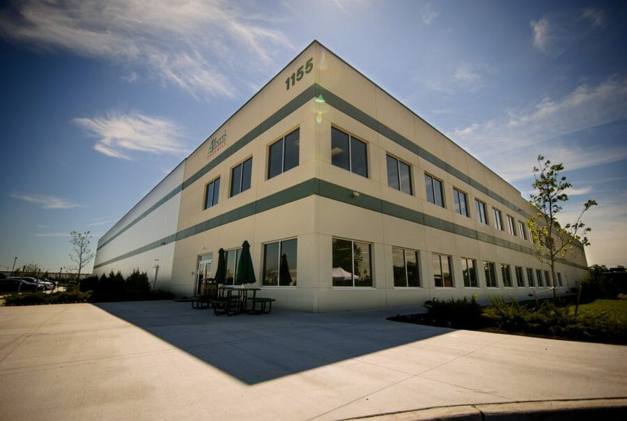Modern two-story industrial building with green accents and a patio under a blue sky.