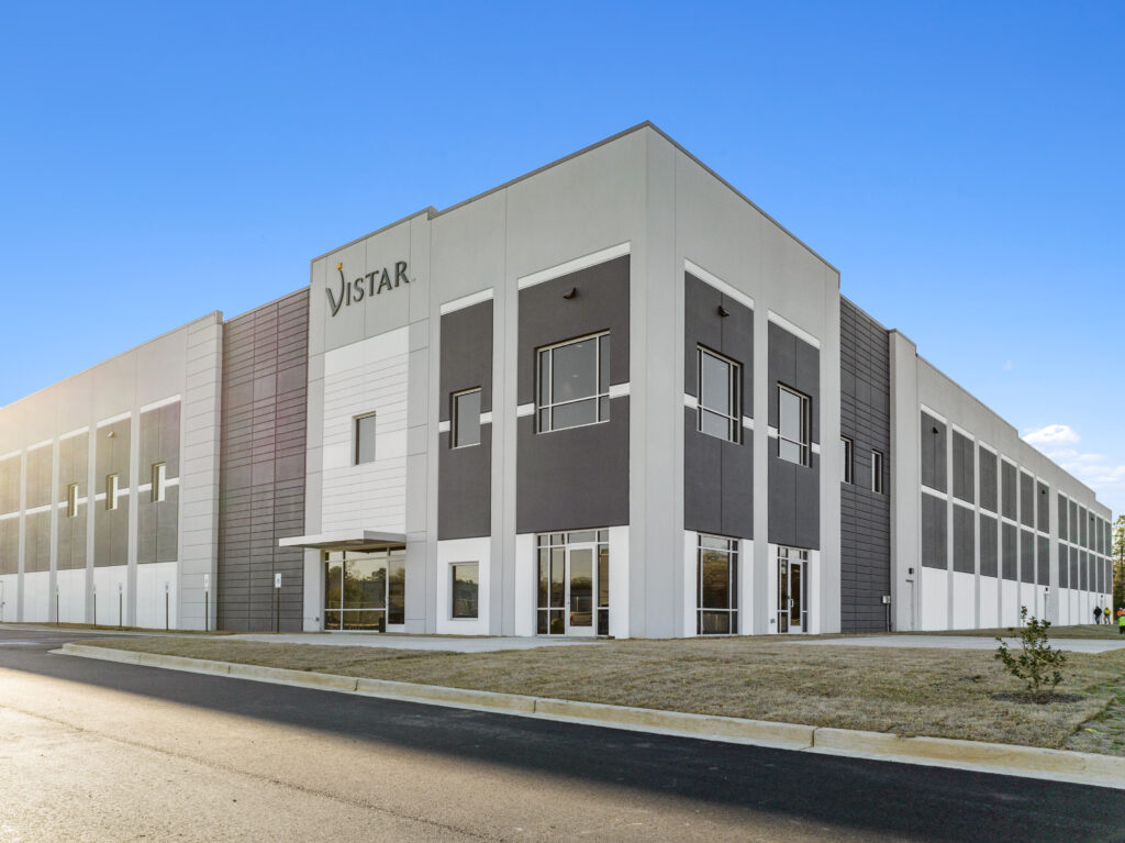 Modern warehouse building featuring gray and white facade, large windows, and clear blue sky background.