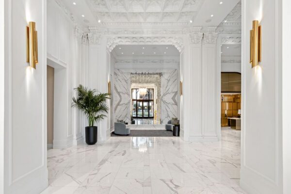 Restored lobby corridor with white marble floors, ornate plaster ceiling and brass wall sconces