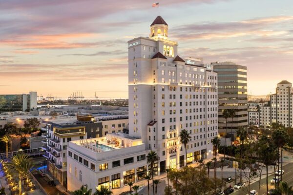 Historic high-rise hotel lit at dusk after restoration, with a new rooftop pool terrace below