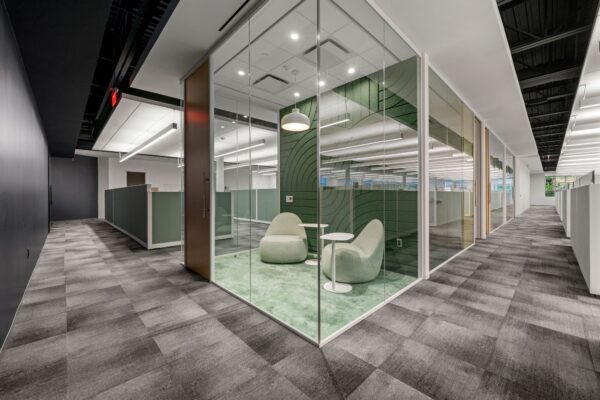 Glass-enclosed huddle room with lounge seating and a curved graphic wall on an open office floor