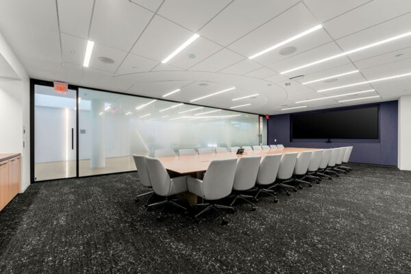 Boardroom with a long conference table, mesh chairs and a wall-width display