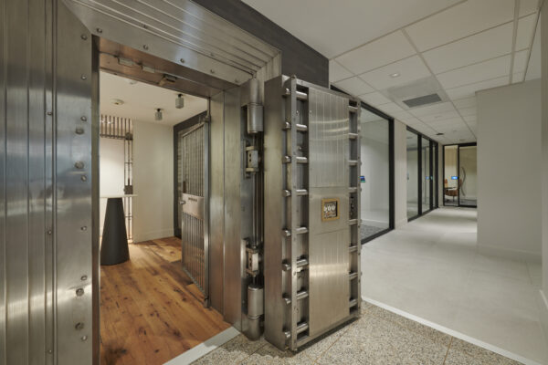 Preserved bank vault door opening into a wood-floored private room off a modern corridor