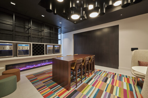 Hotel lounge with a communal table, linear fireplace and a multicolored striped carpet