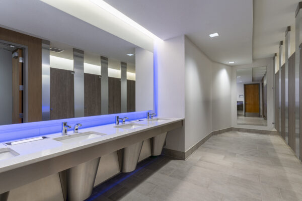 Office restroom with a trough sink, backlit mirror and floor-to-ceiling privacy partitions